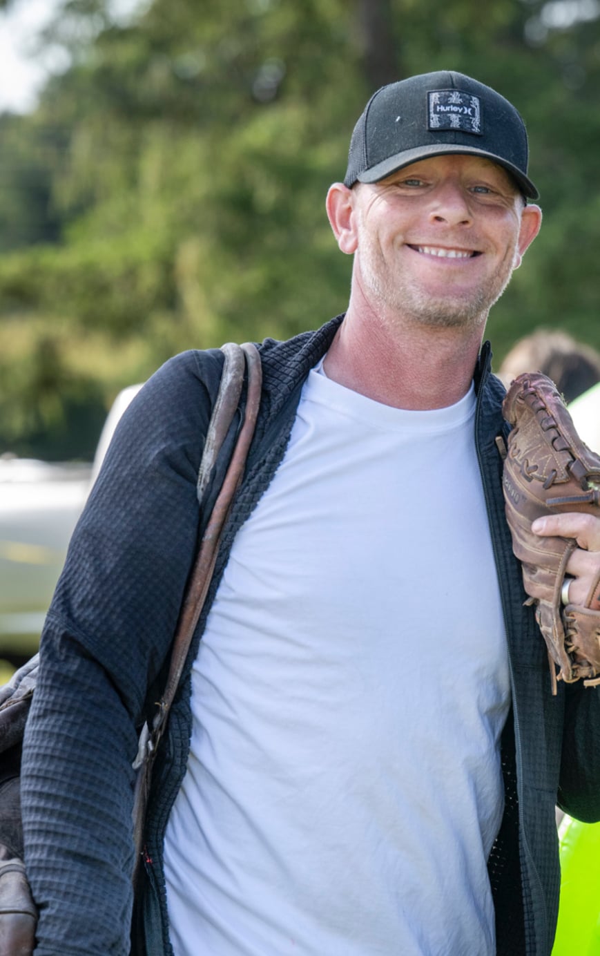 Trent, founder of GlowBall Nation, smiling in a ballcap and holding a baseball glove on the field